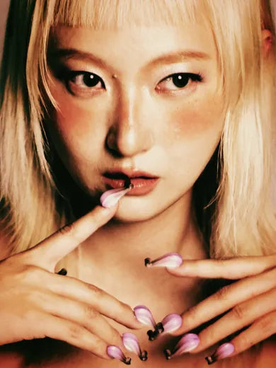 Gia Wang, founder of AuriGia, her fingertips at her lips in pink sculpted nails.