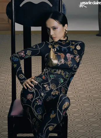 A Marie Claire cover: a model seated in a carved chair, in a black dress embroidered with flowers.