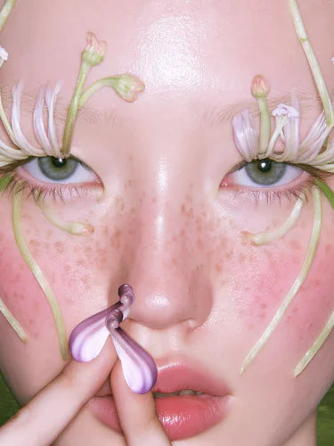 A close crop of the model's face, a Cobaea ring held against her lips.