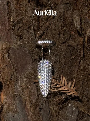 A pavé Glint fingertip ring hanging against dark tree bark beside a sprig of dried needles.