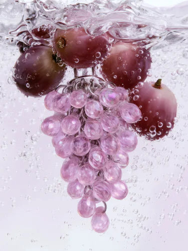 A pink Pistil cluster dropping through water beside grapes, trailing bubbles.