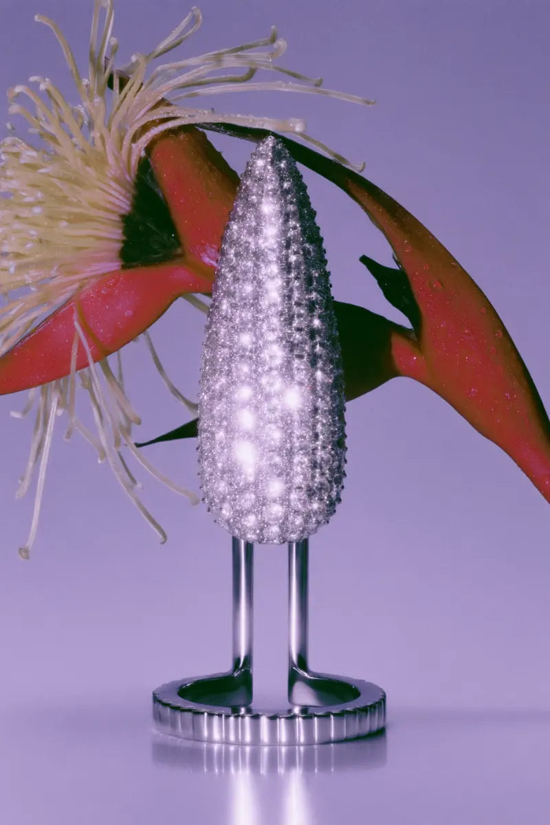 A pavé Pistil fingertip ring on a polished stand against lilac, a red flower opening above it.