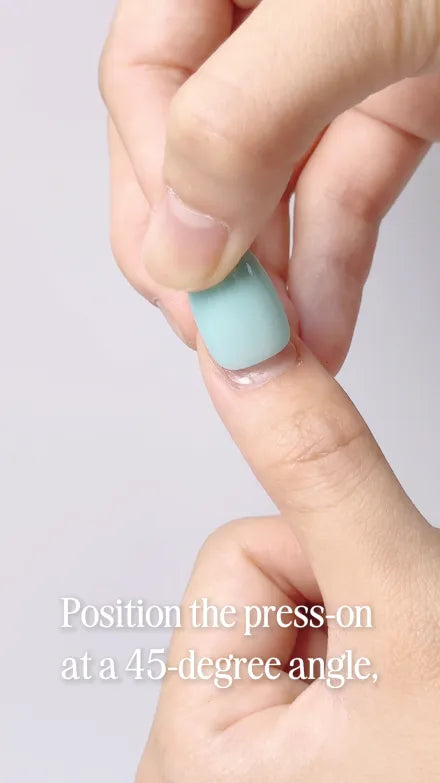 Step 7 of 10. Position the press-on at a 45-degree angle — a mint press-on held to the cuticle end of the nail.