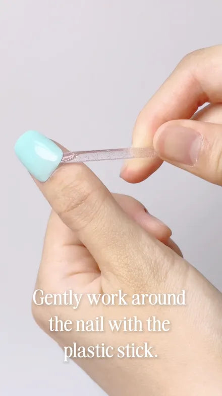 Step 1 of 4. Gently work around the nail with the plastic stick — the cuticle stick easing under the edge of a mint press-on.