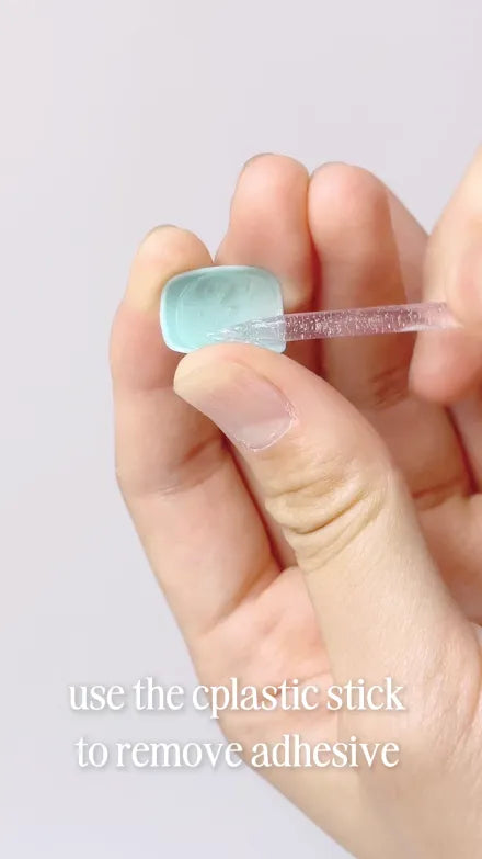 Step 2 of 4. Use the plastic stick to remove adhesive — the old adhesive being pushed off the back of the removed nail.